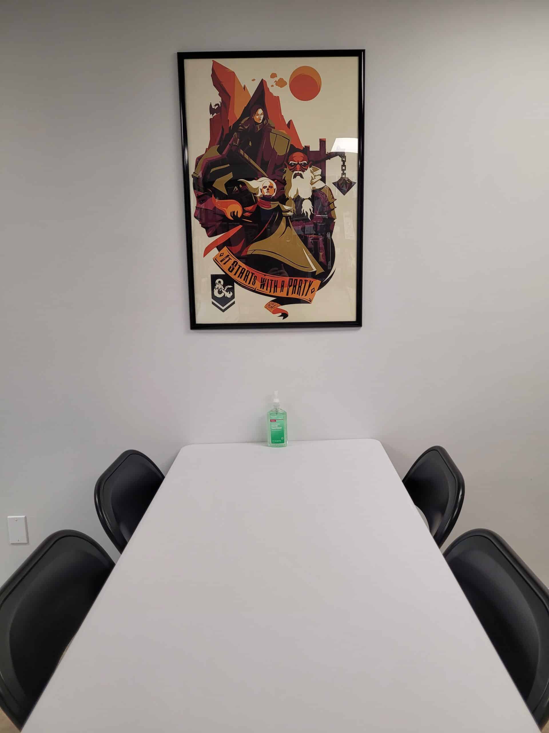 Boardroom meeting room with framed artwork on the wall and a white table with four black chairs.